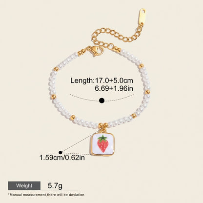 Seraphina Treasures Clytia bracelet with white pearls, gold beads, and a square pendant featuring a red strawberry. Adjustable length.